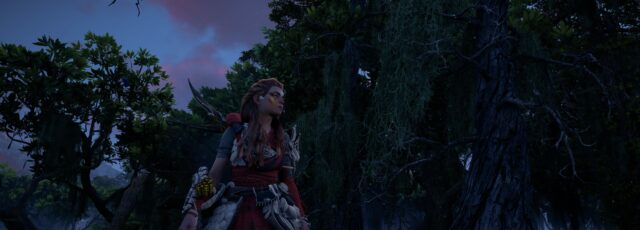 Aloy, the protagonist of the Horizon games, wearing Mark of Pride face paint and red-stained Quen Deadeye armour, stands at sunset in a jungle environment.