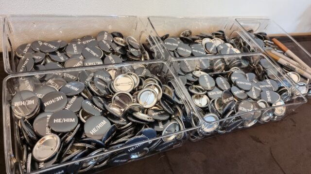 Boxes of pin badges representing various pronouns, plus blank ones and a sharpie.