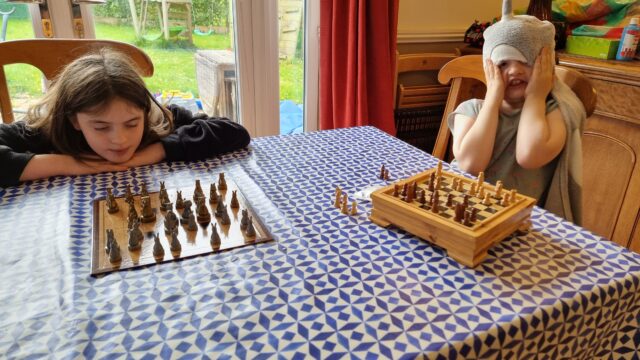 Two frustrated-looking children each sit in front of a separate chessboard (the photographer is presumably playing both of them).