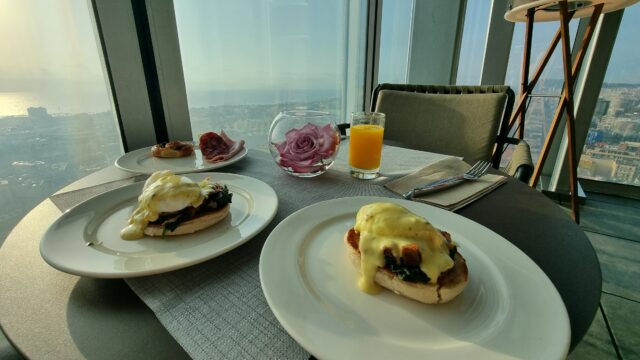 Two portions of eggs benedict, in front of a window showing a 25th-storey view of Barcelona.