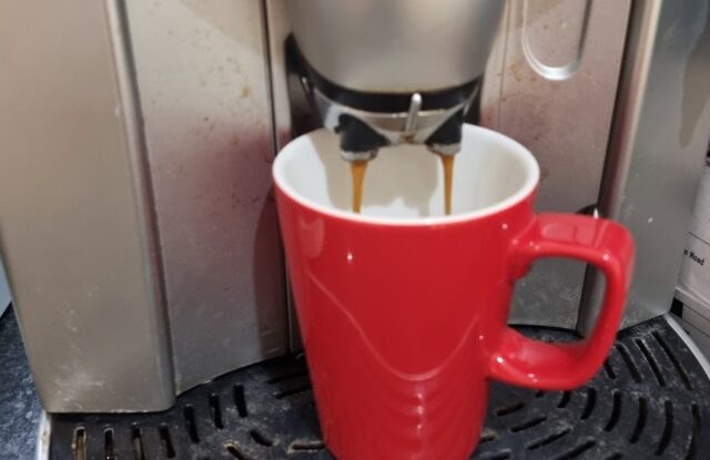 A red mug being filled by a coffee machine.