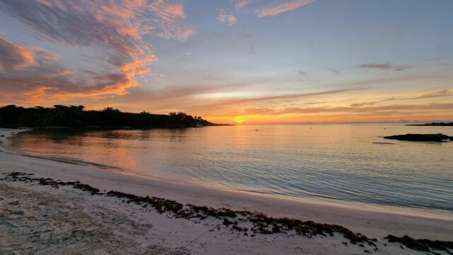 Beautiful sunrise, with reds, oranges, yellows and pinks dappling across the clouds, seen from a Caribbean beach.