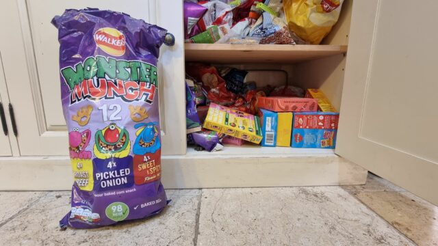 Snack cupboard next to a 12-pack of Monster Munch featuring three flavours: Roast Beef, Flamin' Hot, and Pickled Onion.