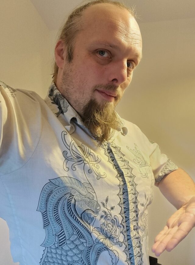 Dan wearing an off-white shirt decorated with intricate inky designs reminiscent of dragons.