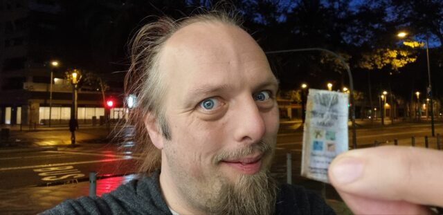 Dan, on a pre-dawn city street, smugly shows the front cover of a little-finger-sized geocaching logbook.