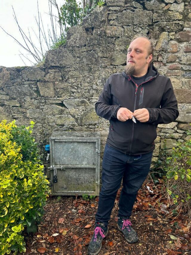 Dan unrolls a cache log while standing in a flowerbed.