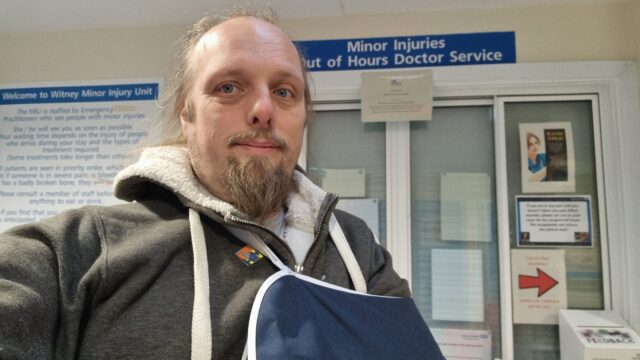 Dan, wearing a sling, stands near the reception of a Minor Injuries Unit.