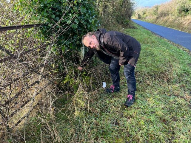 Dan reaches behind a fence post.