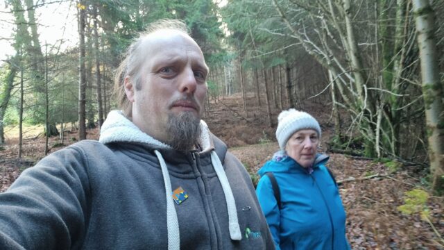 Dan looks concerned next to his mother, in a forest.