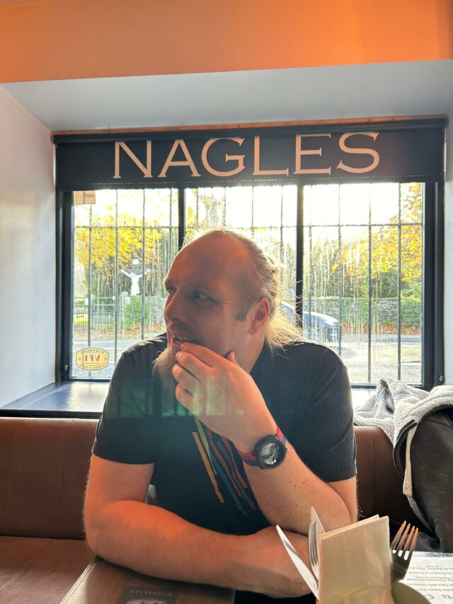 Dan sits in a bar; the word 'Nagles' is over his head on a sign.