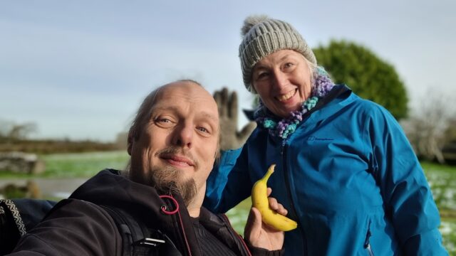 Dan and his mother smiling in a field. Dan is holding a banana.