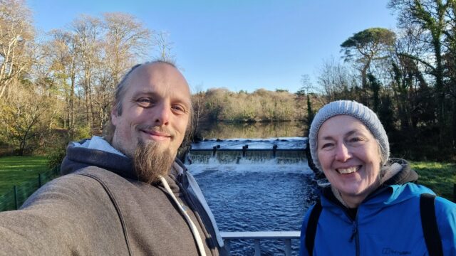 Dan and his mother stand on a bridge with a weir behind them.