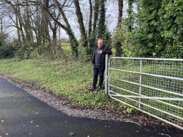 Dan leans against the post of an open metal gate.