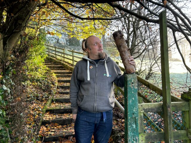 Dan stands by some steps in a park, holding a strange-looking log.