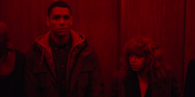 Screengrab from the third episode of Russian Doll, showing Alan (Charlie Barnett) and Nadia (Natasha Lyonne) standing in a lift whose red emergency lights have come on.