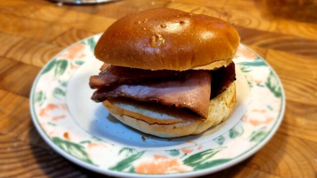 Brioche bun loaded with thick cut bacon rashers, plated, on a wooden surface.