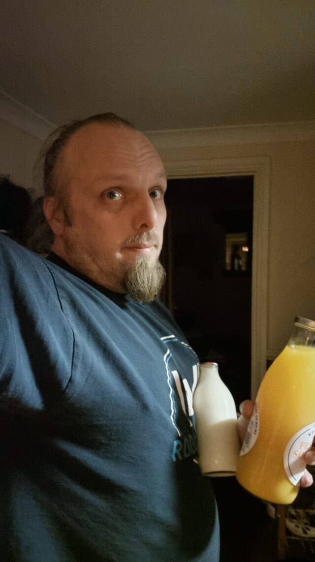 Dan,looking tired, holds glass bottles of orange juice and of milk.