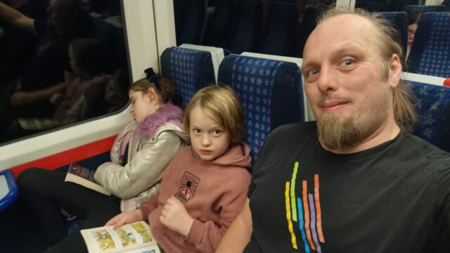 Dan sits on a train alongside a boy and a sleeping girl.