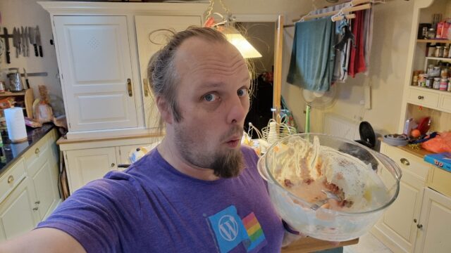 Dan, standing on a kitchen, holds a large bowl partially filled with trifle.