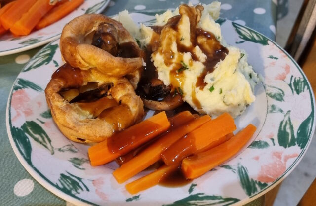 A pyramid of four bite-sized toads-in-the-hole alongside chive mash and carrots, smothered in gravy, on a plate.