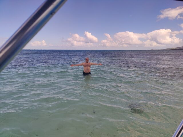 Dan stands waist-deep in seawater; land is visible in the far distance.