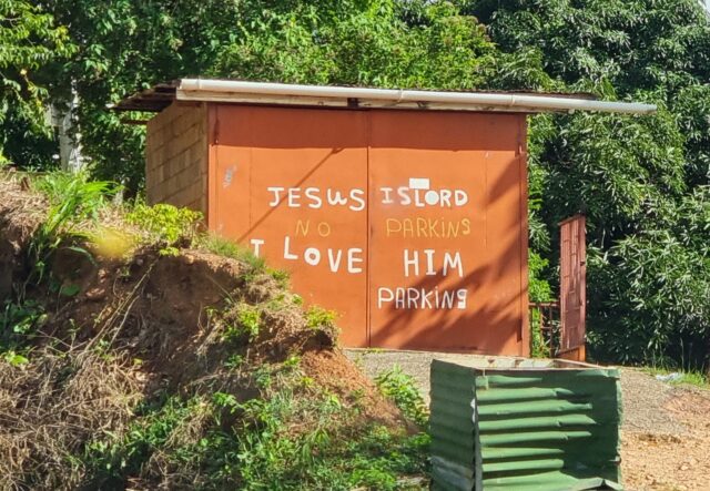 Orange garage on a tropical hillside, on the front of which are painted the words: 'Jesus is Lord. I love him.' And then below and between those lines: 'No parking'.