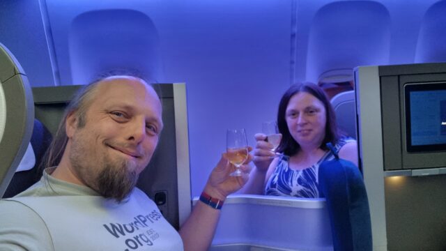 Dan and Ruth clink champagne glasses between the booths of their club class seats.