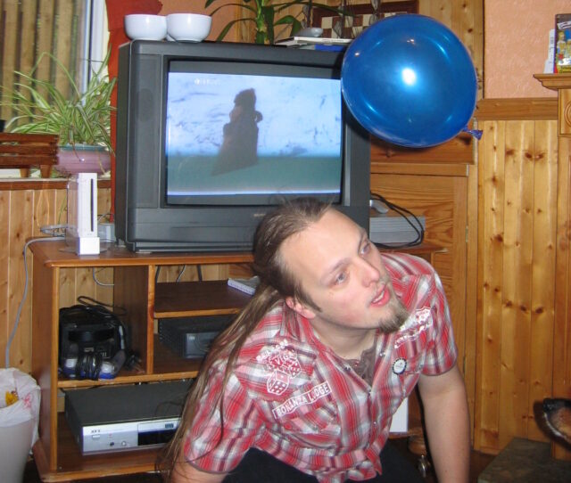 Dan, in his 20s, crouches awkwardly in front of a TV and a Nintendo Wii in a wood-panelled room as he attempts to headbutt a falling blue balloon.