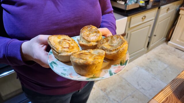 Plate containing four beautifully-browned but slightly lopsided pies, held in a woman's hands.