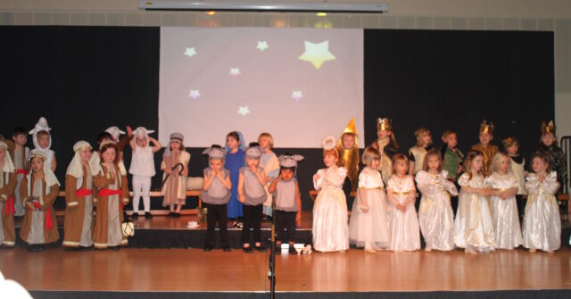 A group of children dressed as Mary, Joseph, shepherds, kings, angels, and a variety of barn animals crowd a stage.