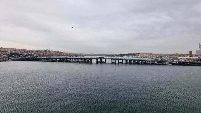 View from above a river, flanked by dense city on both sides, under an overcast sky.