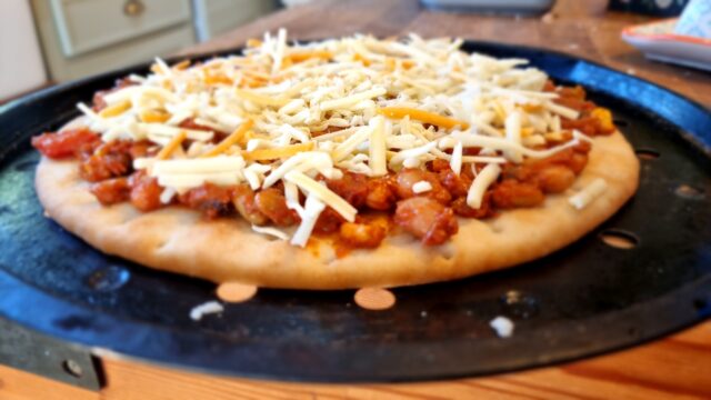 Pizza built with bean chilli and mixed grated cheese, ready to go into an oven.