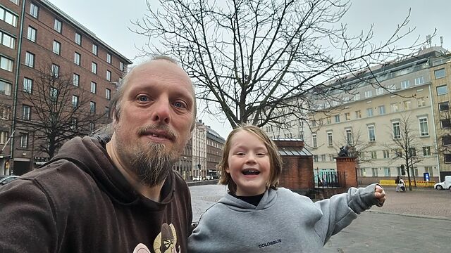 Dan and a young boy pose in front of a statue of two bears, atop a brick plinth in a city square.