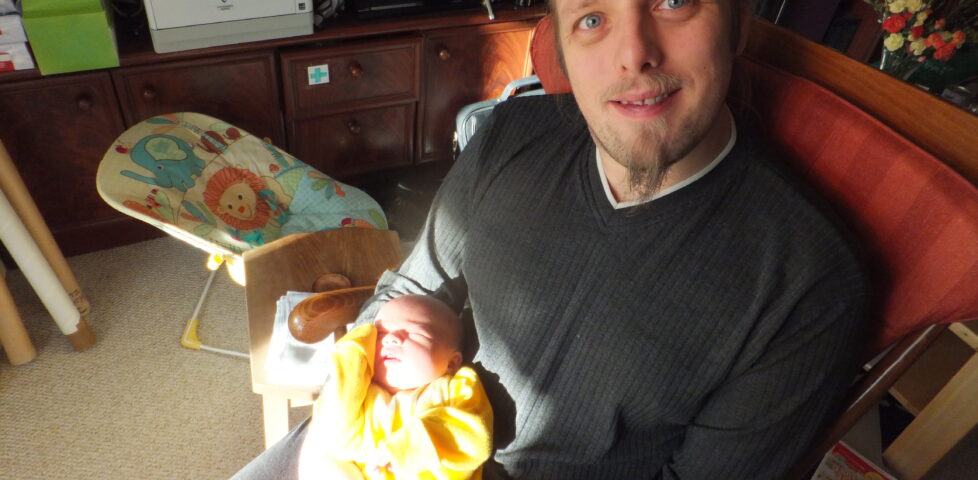 Dan, sitting in the sunlight, rocking the baby.