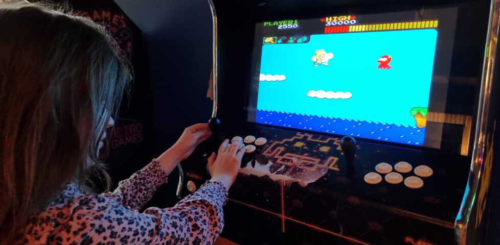 A young girl in a pink leopard-print top plays Wonder Boy on an arcade cabinet.