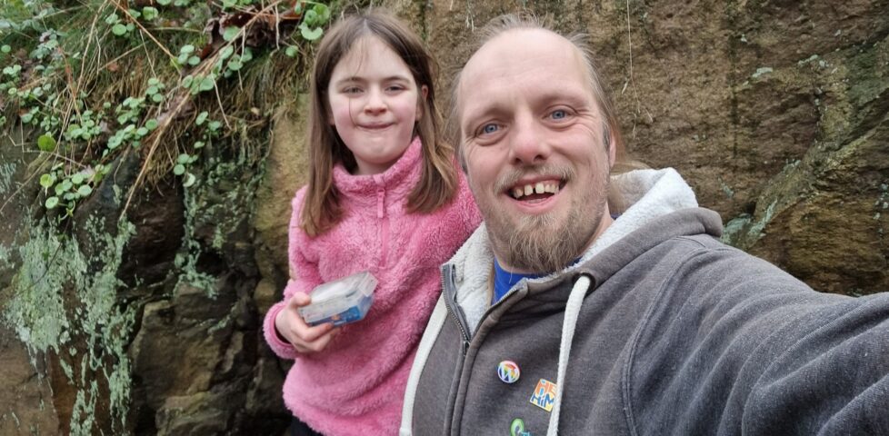 Dan smiles alongside a 10-year-old girl who's holding a geocache container.