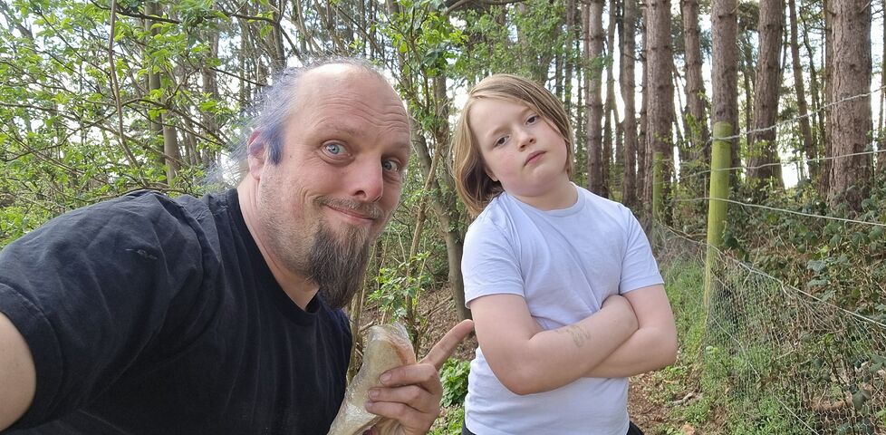 Dan and a boy holding cling-wrapped sandwiches in a forest.