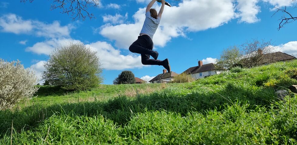 A boy hangs from a rope swing over a grassy hillside.