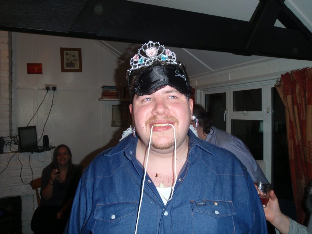 Alec having lost a doughnut-eating competition; still wearing the blindfold, tiara, and earrings from two previous challenges.