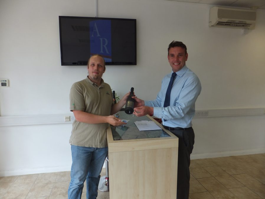 Dan is handed keys and a bottle of sparkling wine by Mark, the estate agent.
