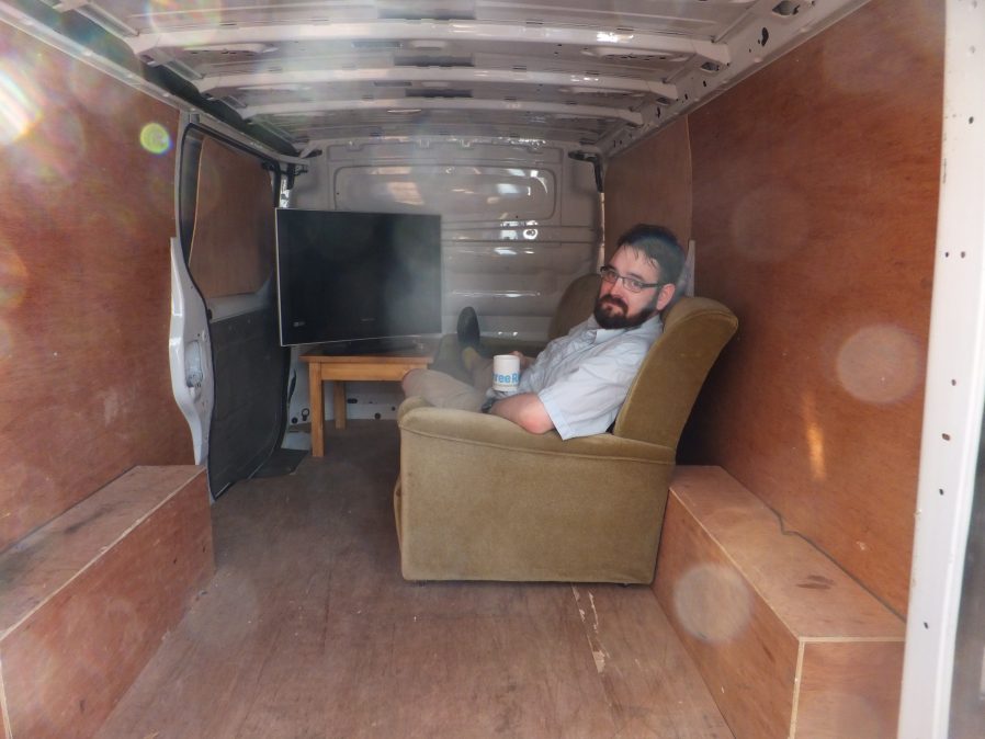 JTA in the back of the van, in which a small mock living room has been assembled.