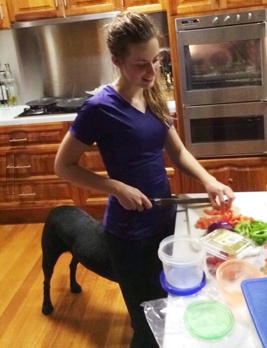 Woman cutting vegetables with dog behind; from this angle, she looks like a centaur.