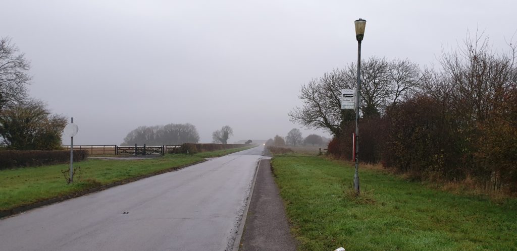 Bus stop attached to a lamppost on a misty, empty road.