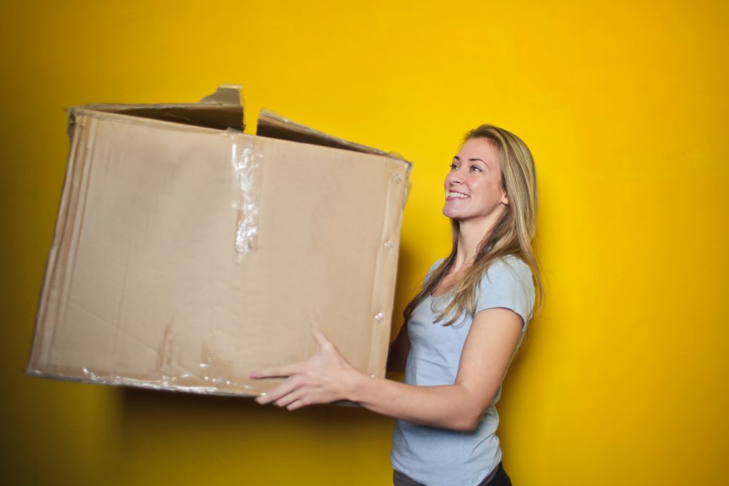 A woman carries a large cardboard box.