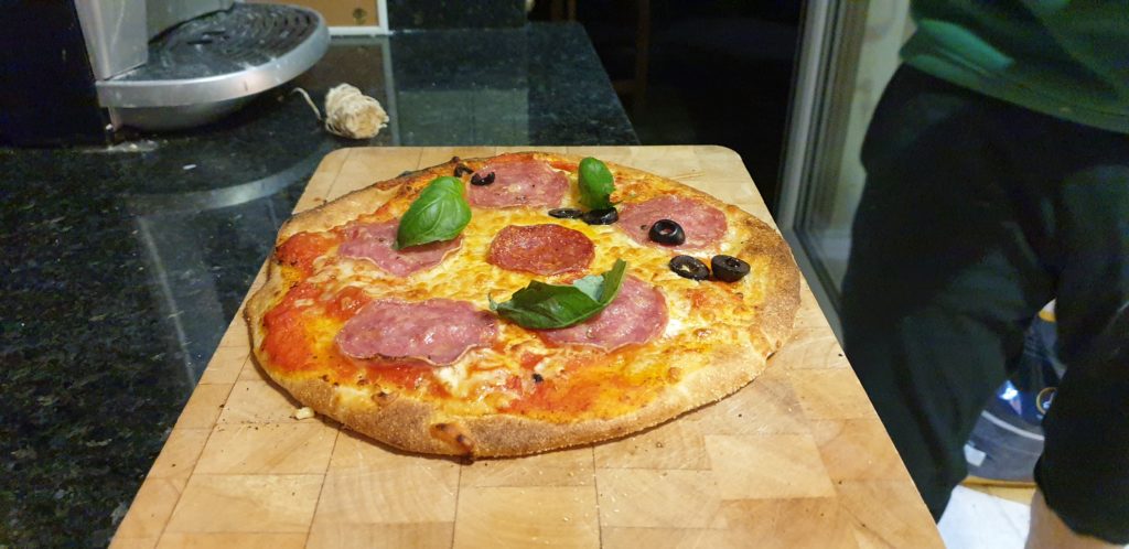 A salami and basil pizza with olives on half.