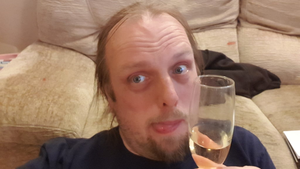 Dan with his tongue out holding a glass of champagne.