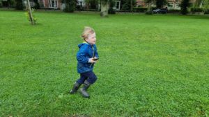A boy, holding a GPS receiver, runs across a park lawn.