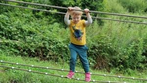 A boy climbs a two-rope crossing, balancing on the bottom rope while holding the top rope.