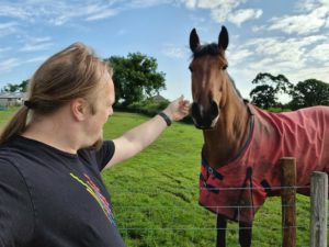 Dan strokes a large brown horse wearing a red jacket.