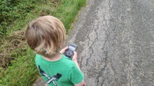 A boy holds a GPS receiver as he walks down a lane.